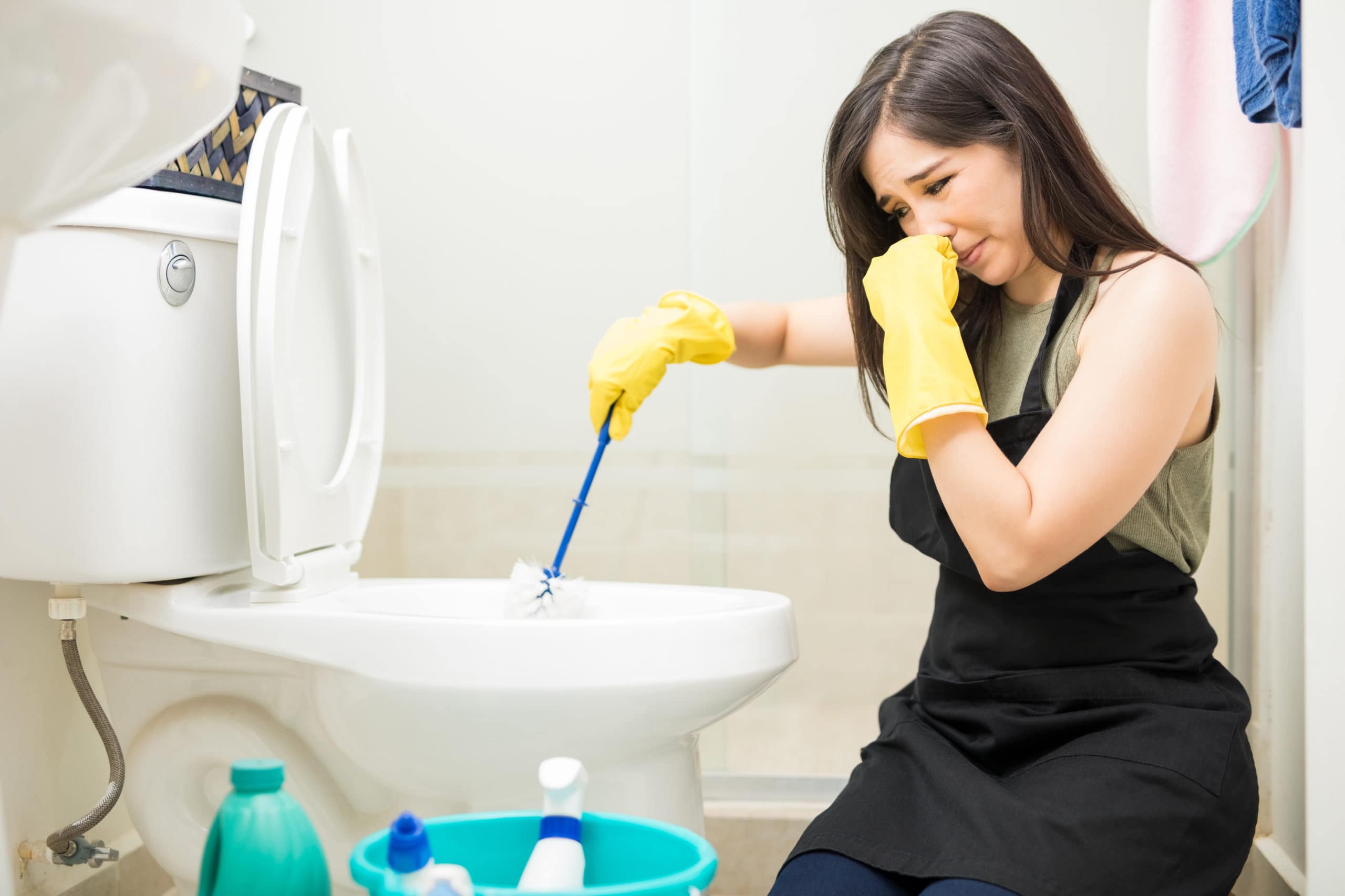 Young woman covering nose to avoid bad smell while cleaning a smelly toilet bowl