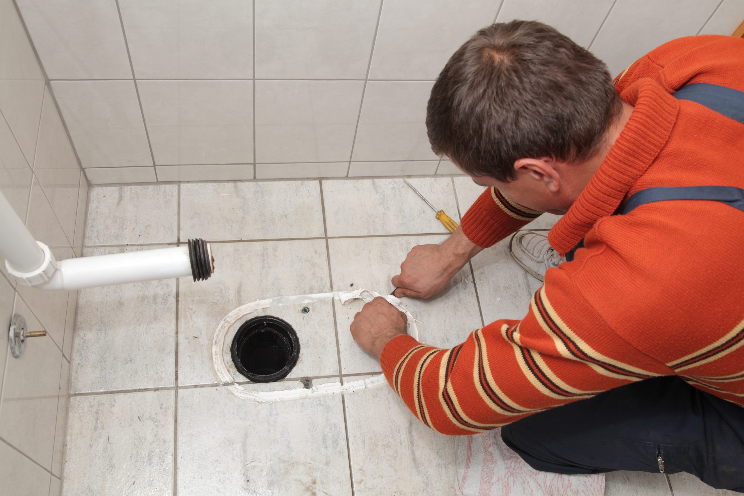 Plumber replacing broken toilet in a washroom, cutting of silicone glue