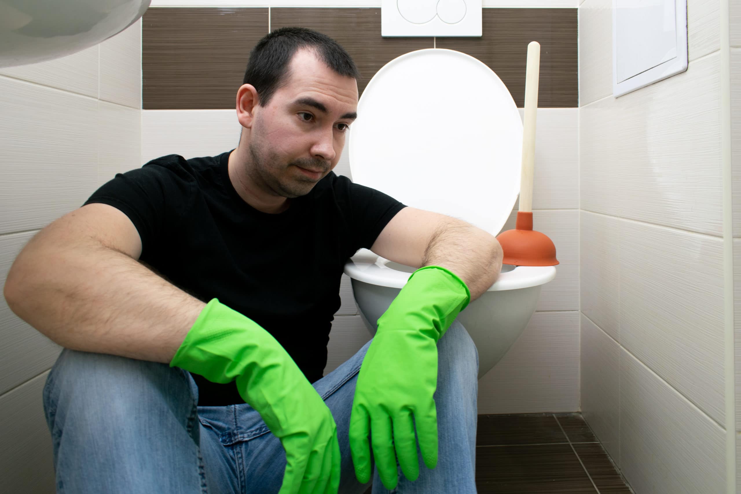 unalbe to solve toilet clog problem , a man sitting on floor feeling unhappy