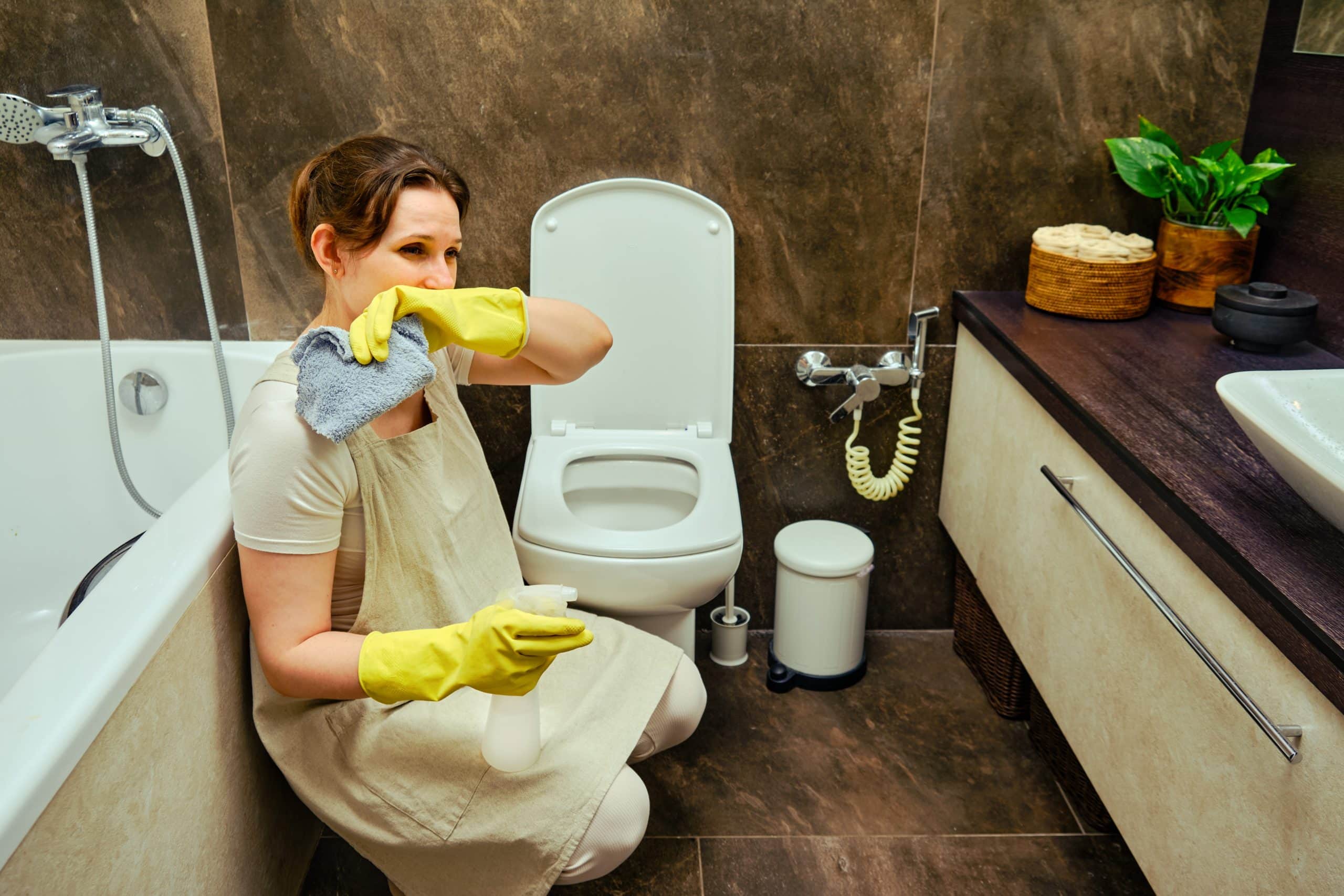 A woman cleans the home bathroom with a sense of disgust at the toilet bowl. Unpleasant odors and aversion to dirt while cleaning.