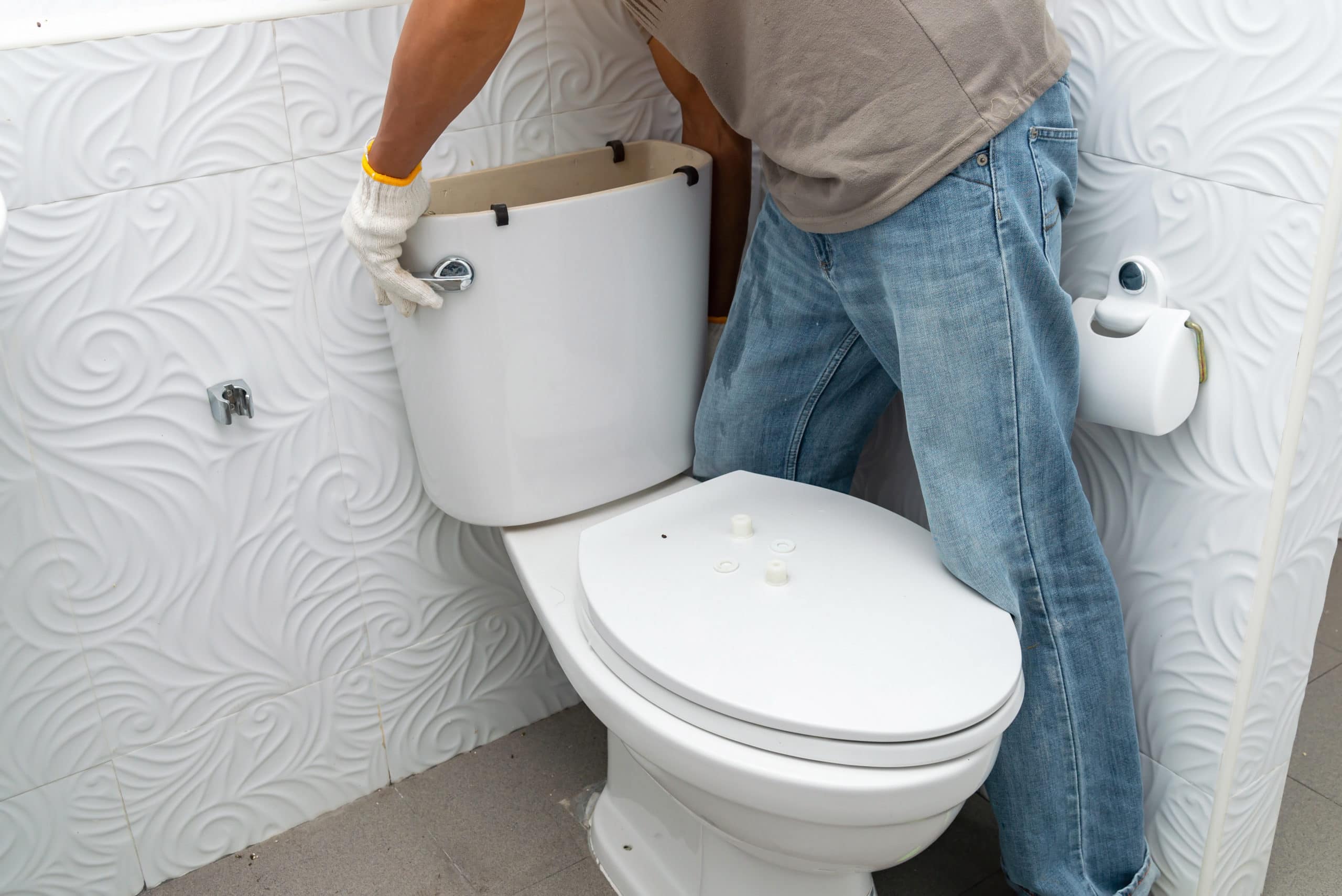 handman removing the toilet tank from toilet