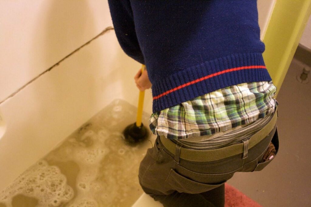 a man using a plunger to clear the drain causing standing water
