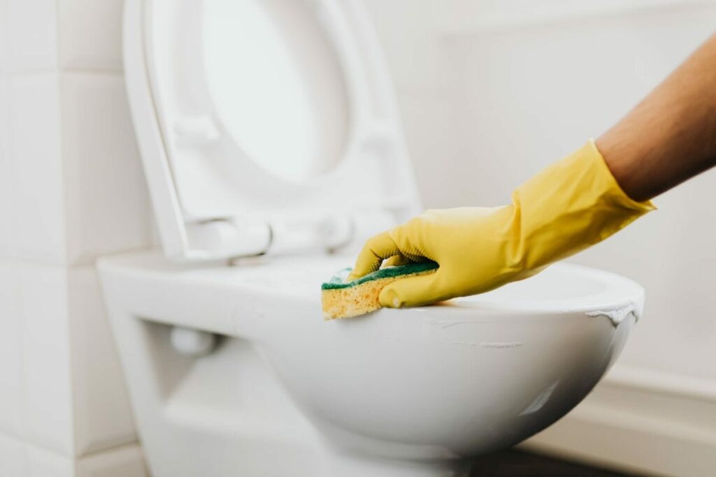 a gloved hand cleaning a porcelain toilet using a sponge