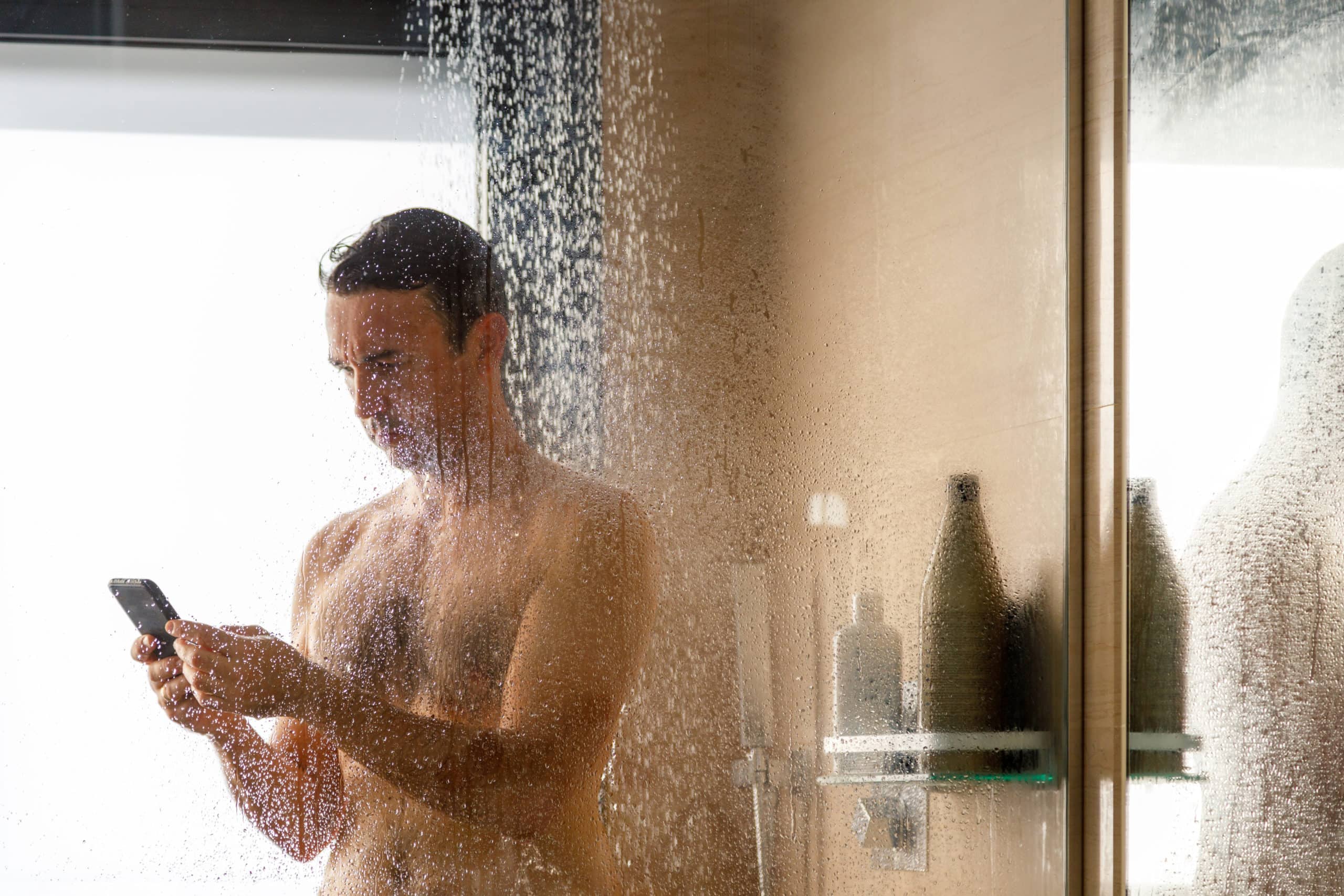 Naked young man showering while using a cell phone