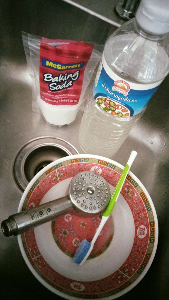 a shower head in the bowl, alongside are toothbrush and baking soda
