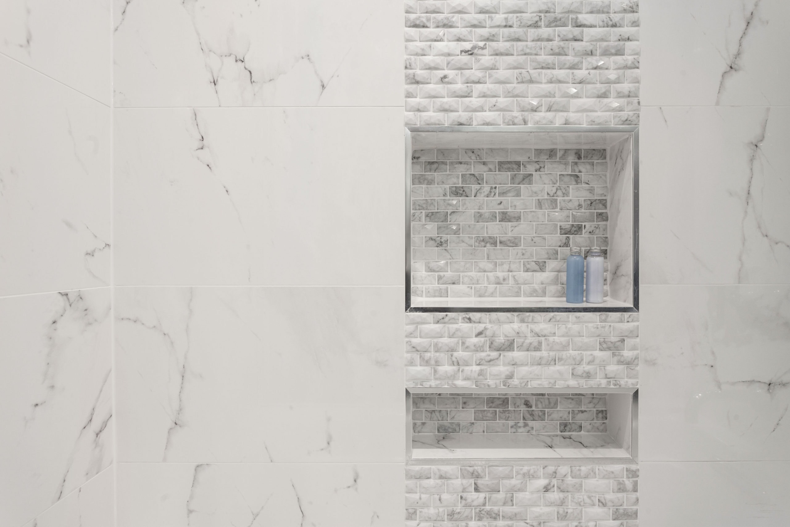 Shampoo and conditioner or shower gel bottles in a rectangular niche made of white mosaic tiles in shower and bathroom.