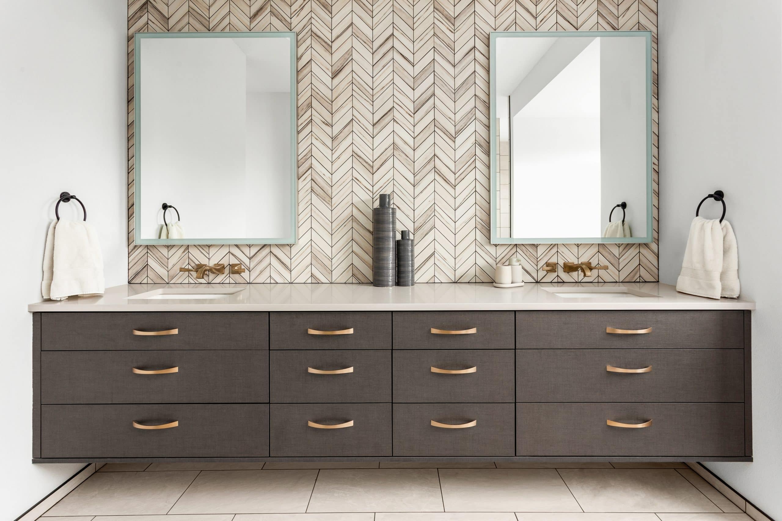 Bathroom in luxury home with double vanity. Features herringbone tile backsplash, quartz countertops, undermount sinks, and floating faucets and cabinets.