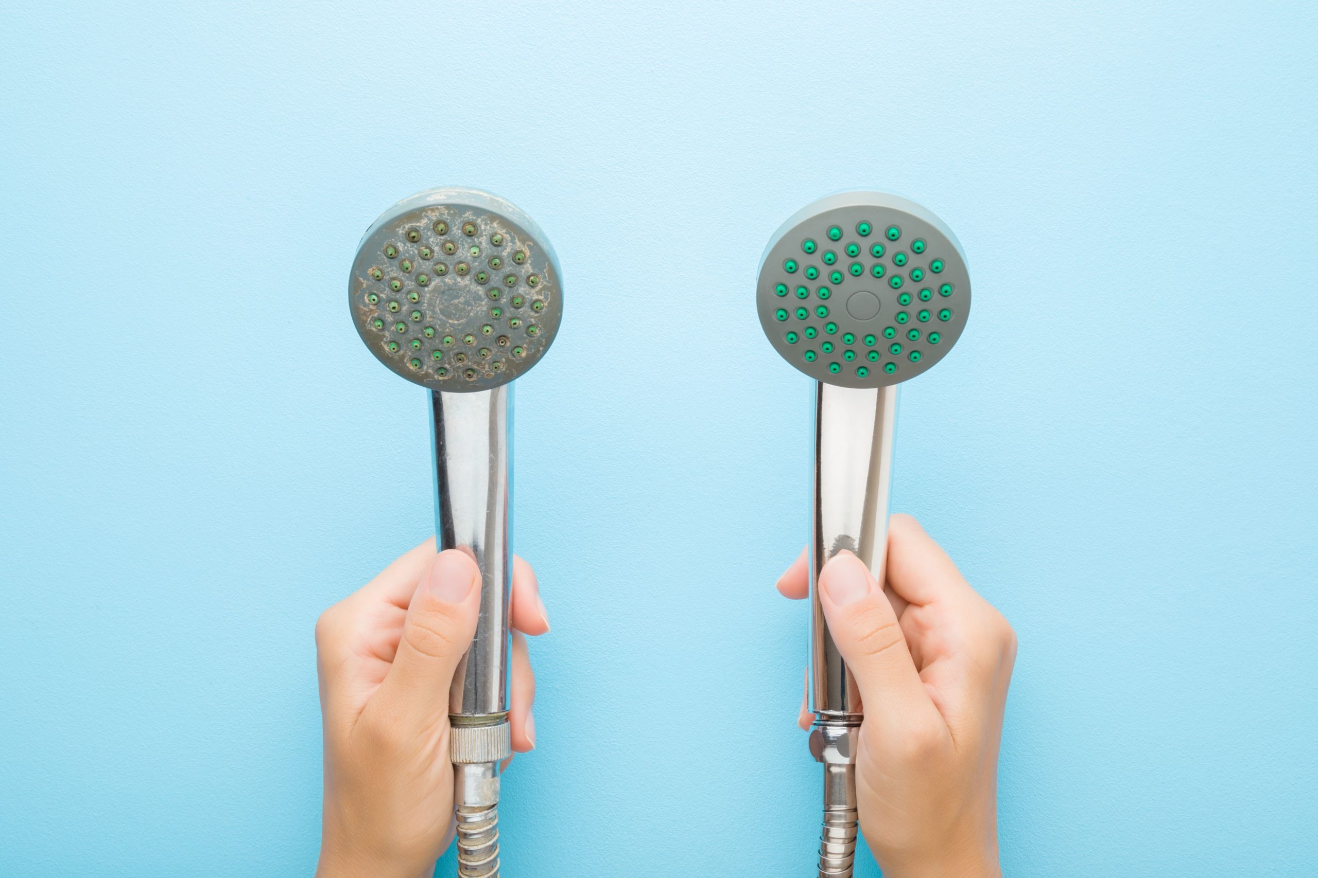 Young adult woman hands holding new and old shower heads on light blue table background.