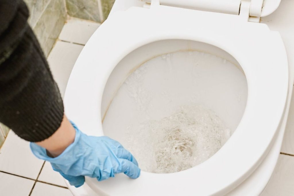 person wearing gloves to get an object in toilet trap